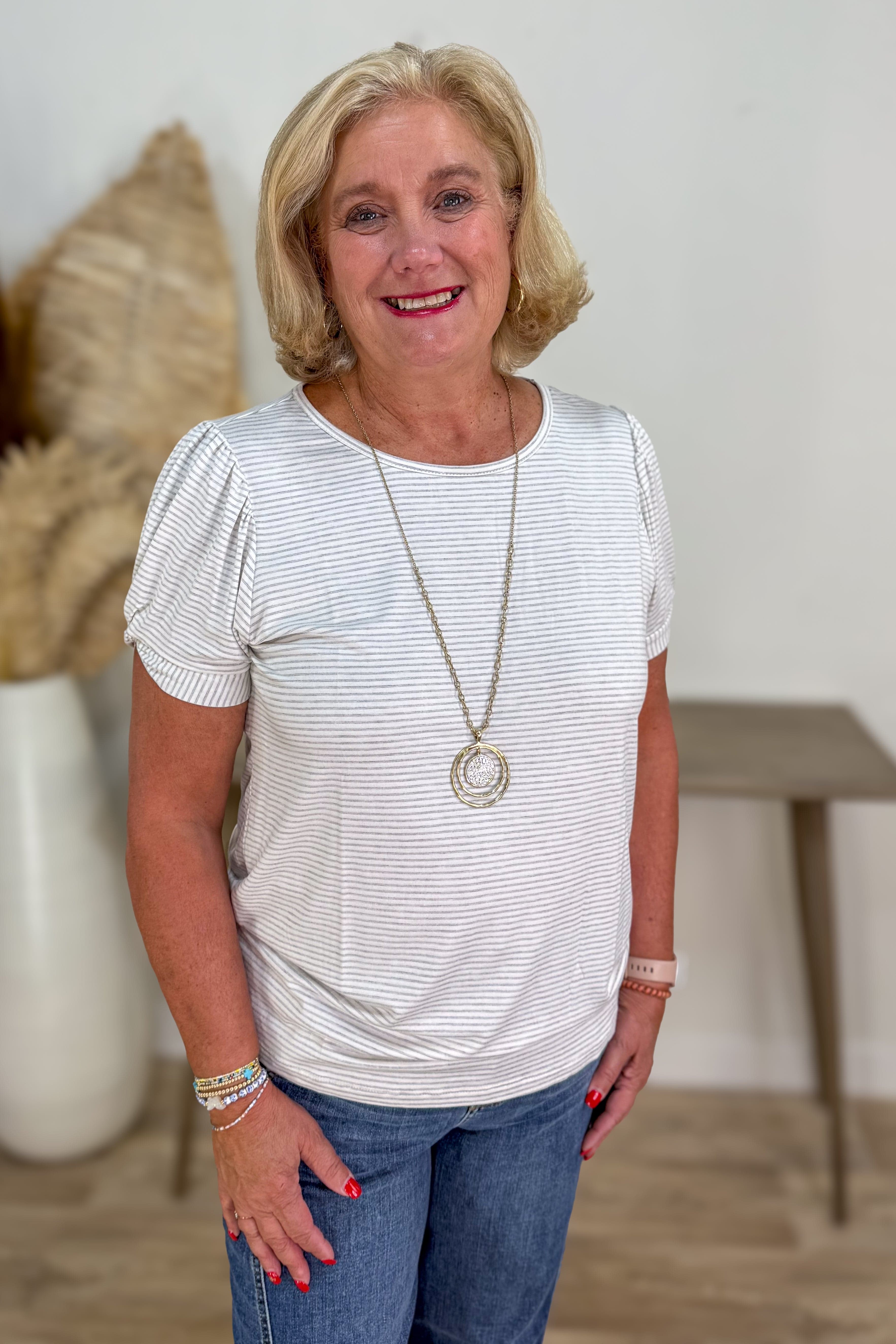 Woman wearing a white striped shirt and blue jeans standing indoors.