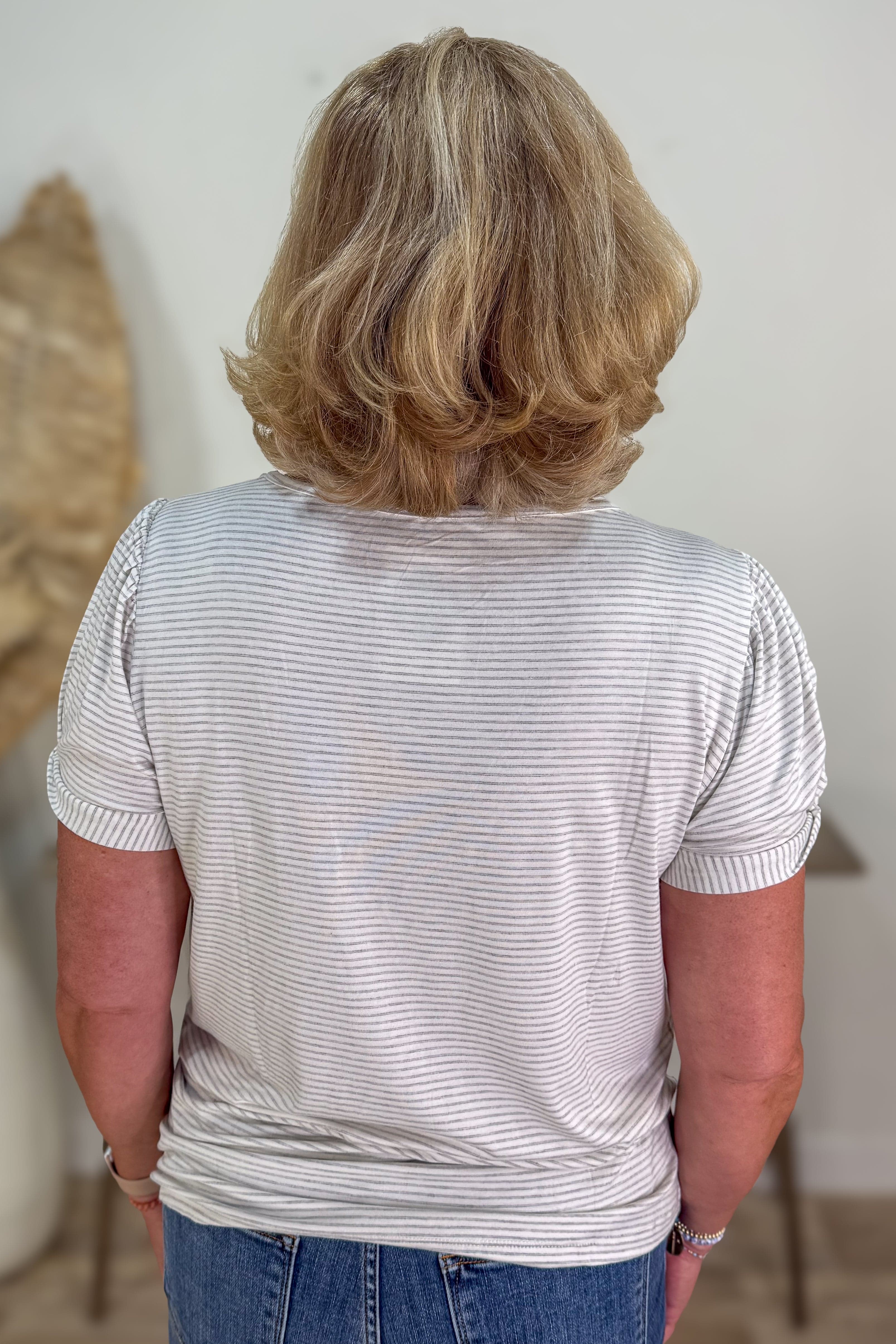 Person wearing a striped shirt and blue jeans with a neutral background