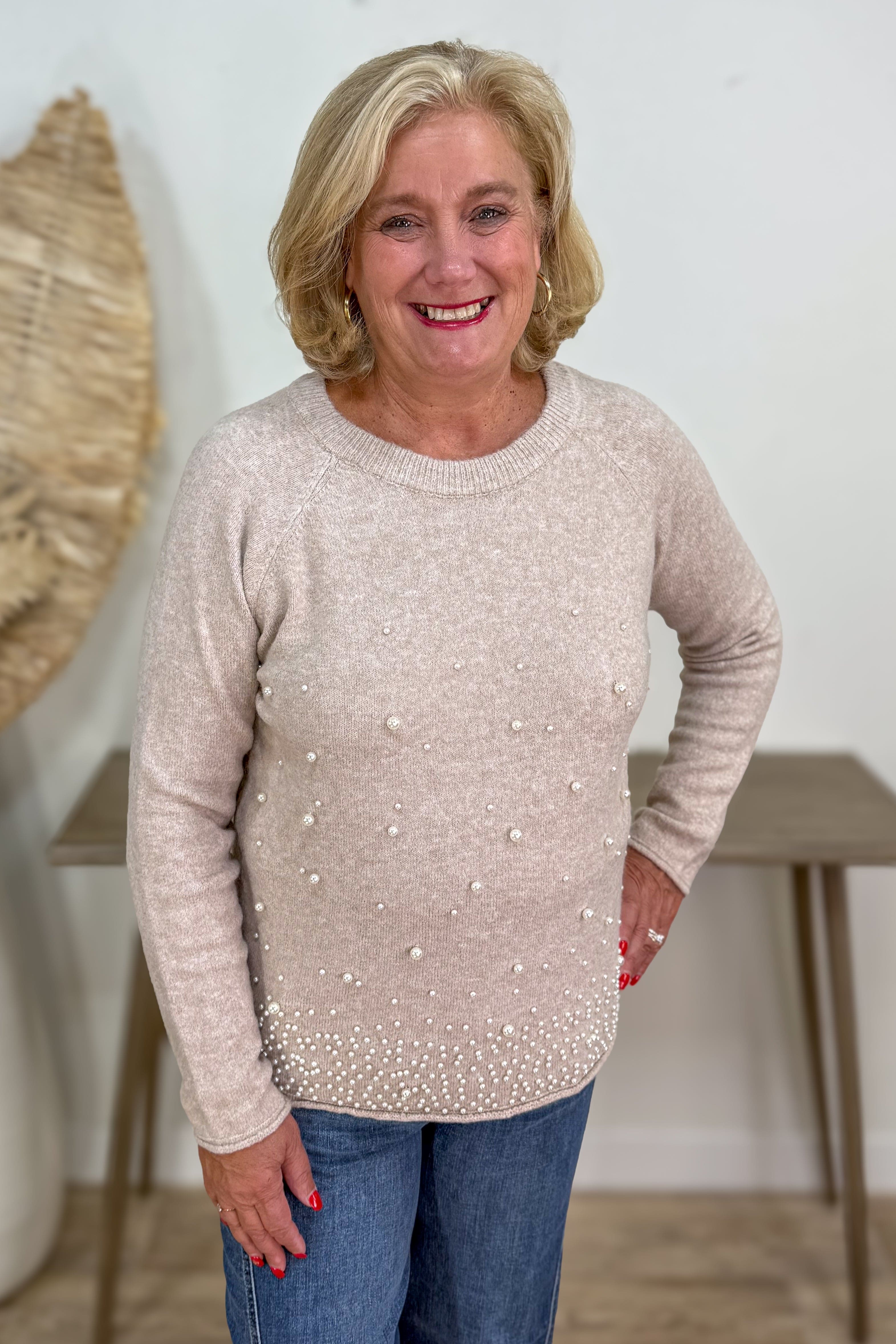 Woman wearing a beige sweater with pearl embellishments indoors.