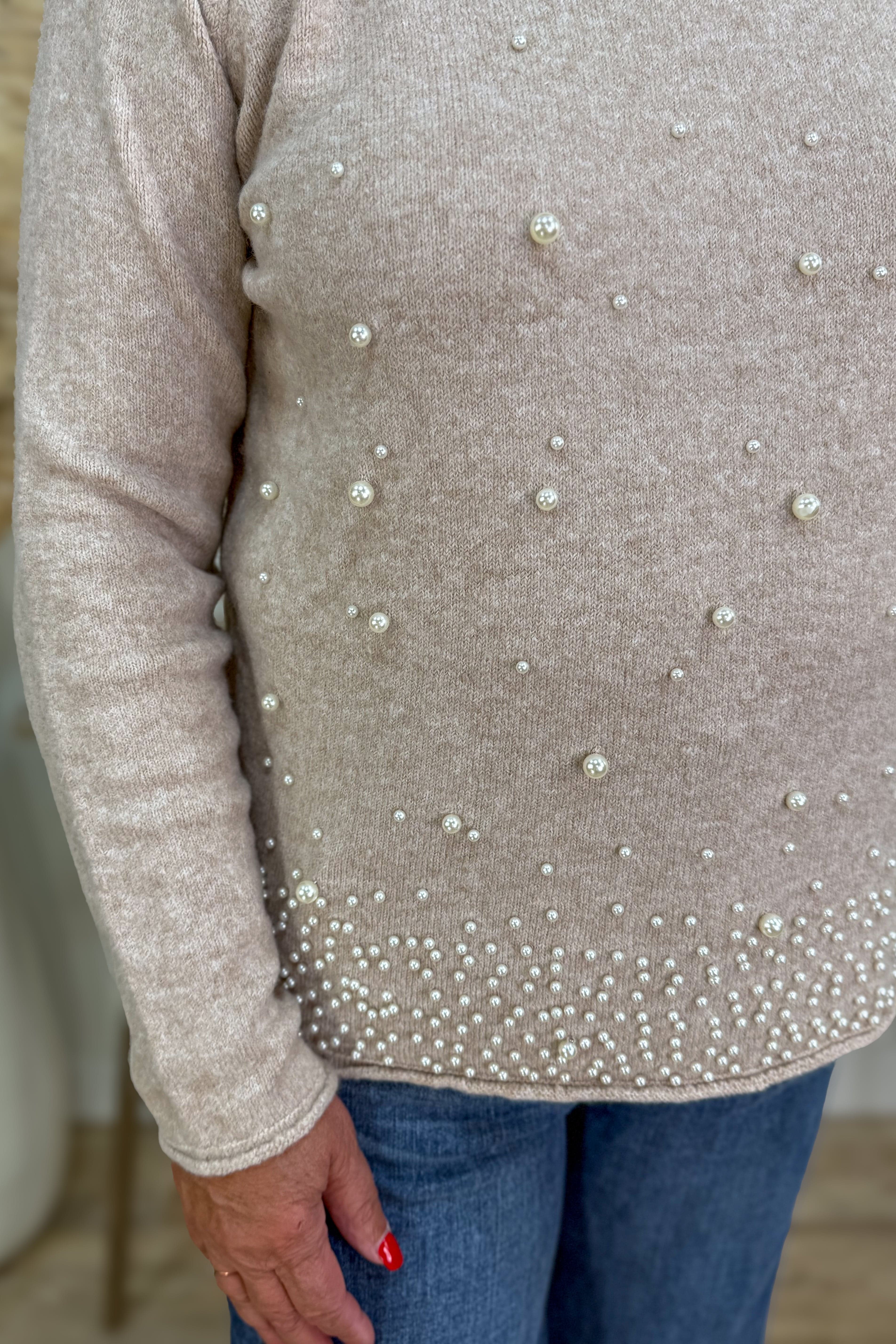 Close-up of a beige sweater with pearl embellishments worn by a person.