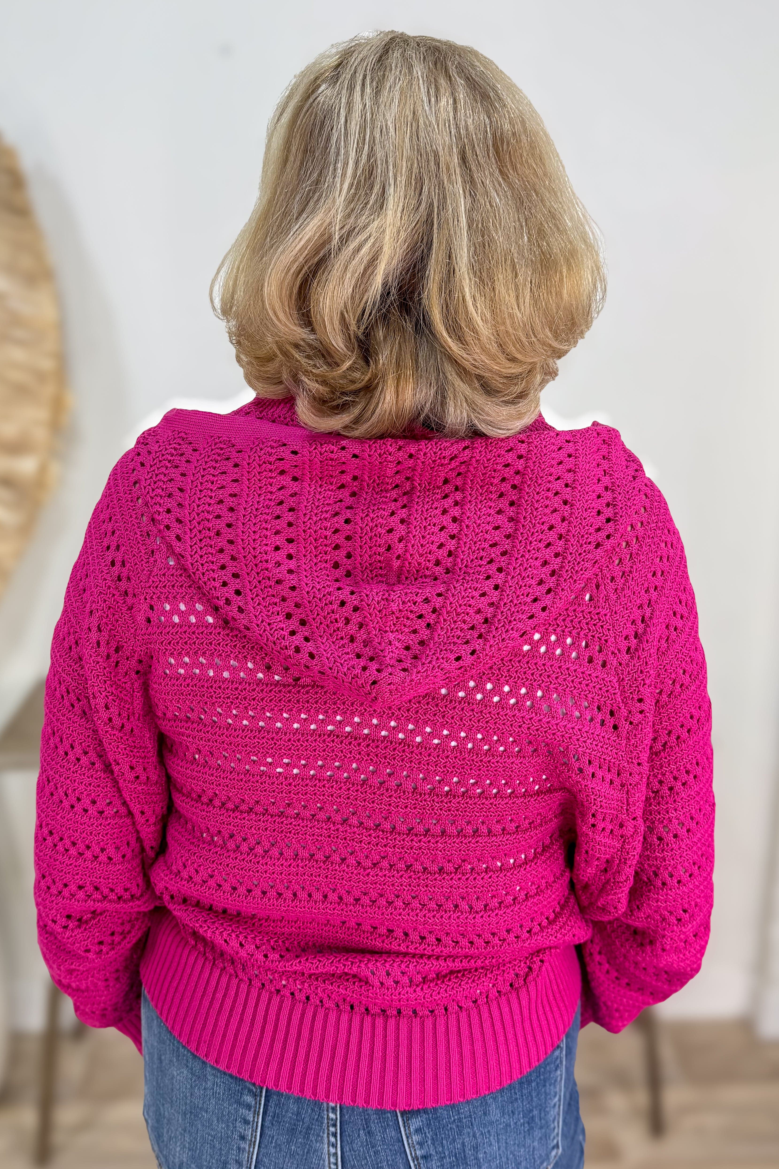 Person wearing a bright pink knitted sweater with a white shirt underneath, standing against a neutral background.