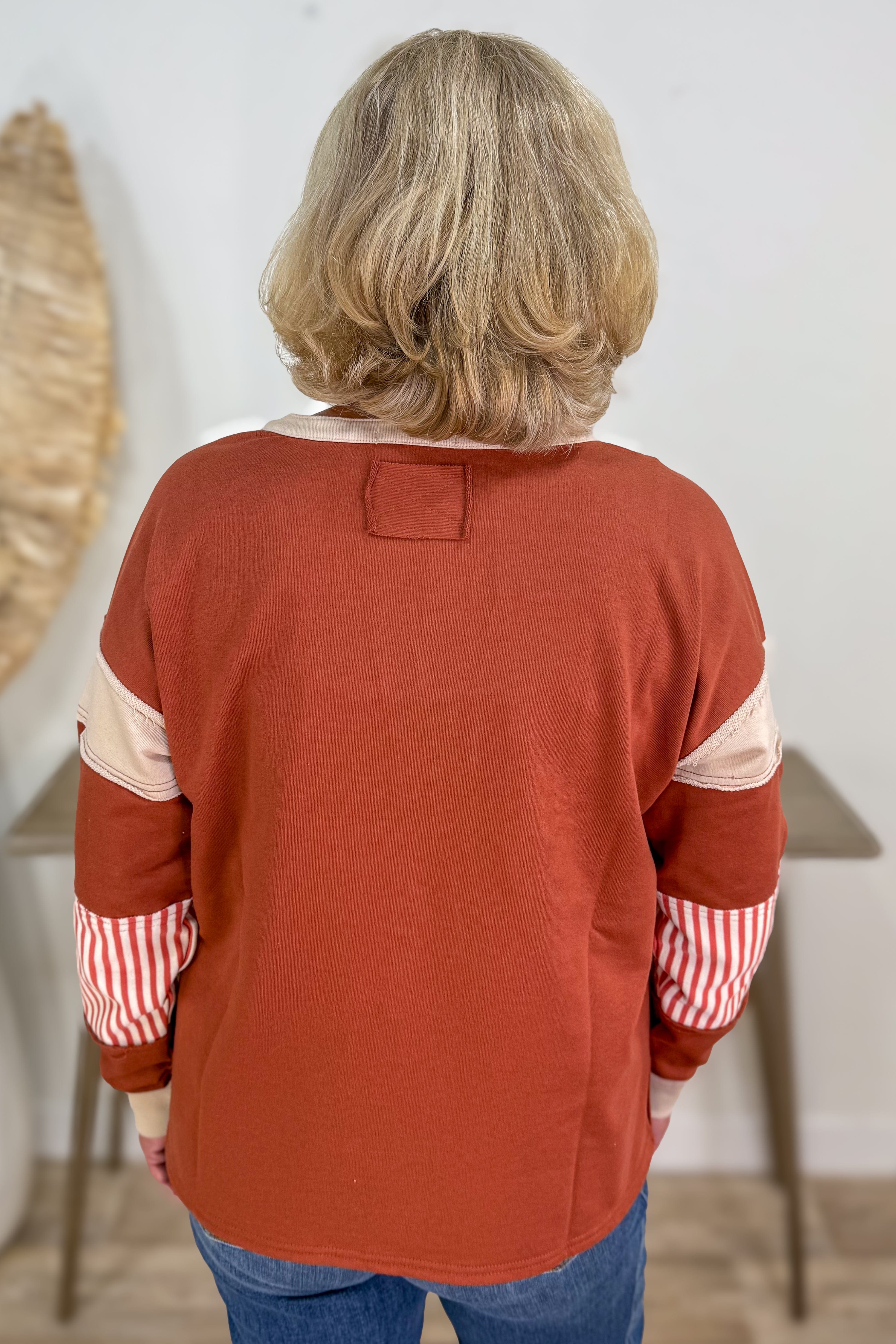 Person wearing a rust-colored shirt with red and white checkered sleeves, standing indoors.