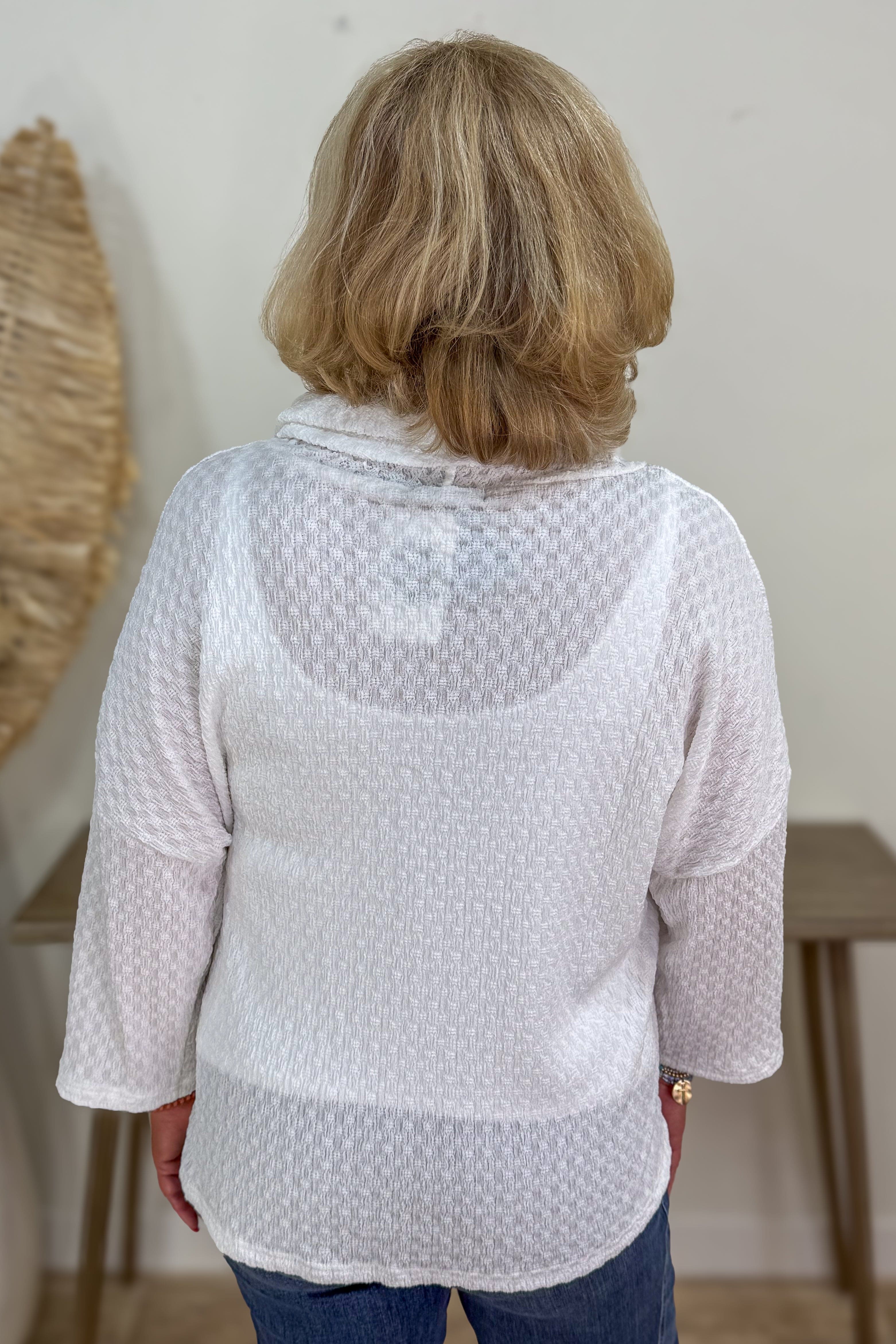 Person wearing a light gray textured blouse with a white wall background