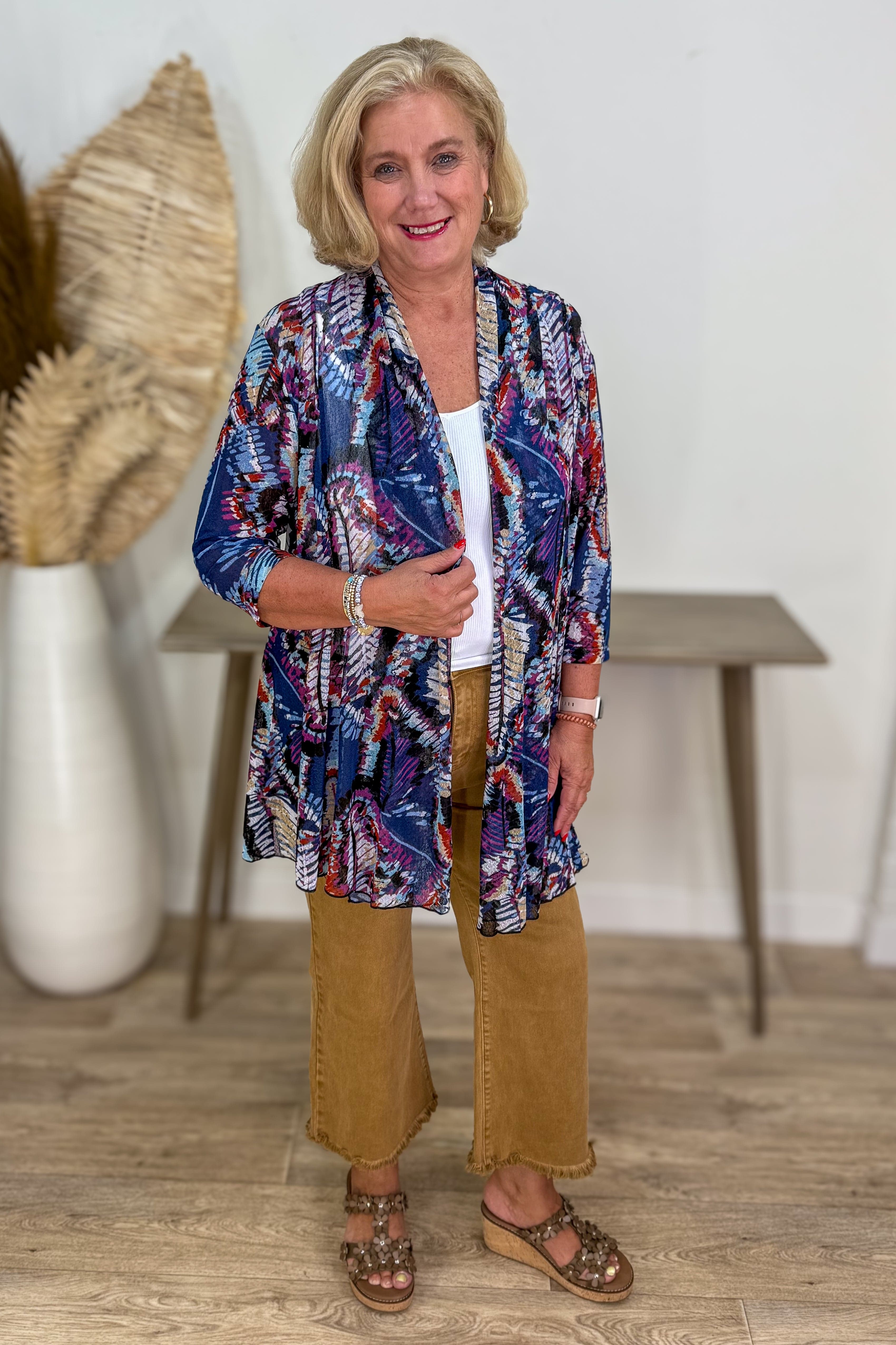 Woman wearing a colorful patterned shirt and beige pants indoors.