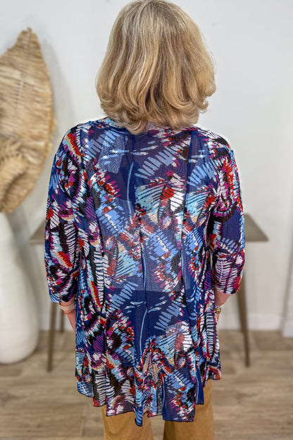 Person wearing a colorful patterned shirt in a room with a white wall and wooden floor.