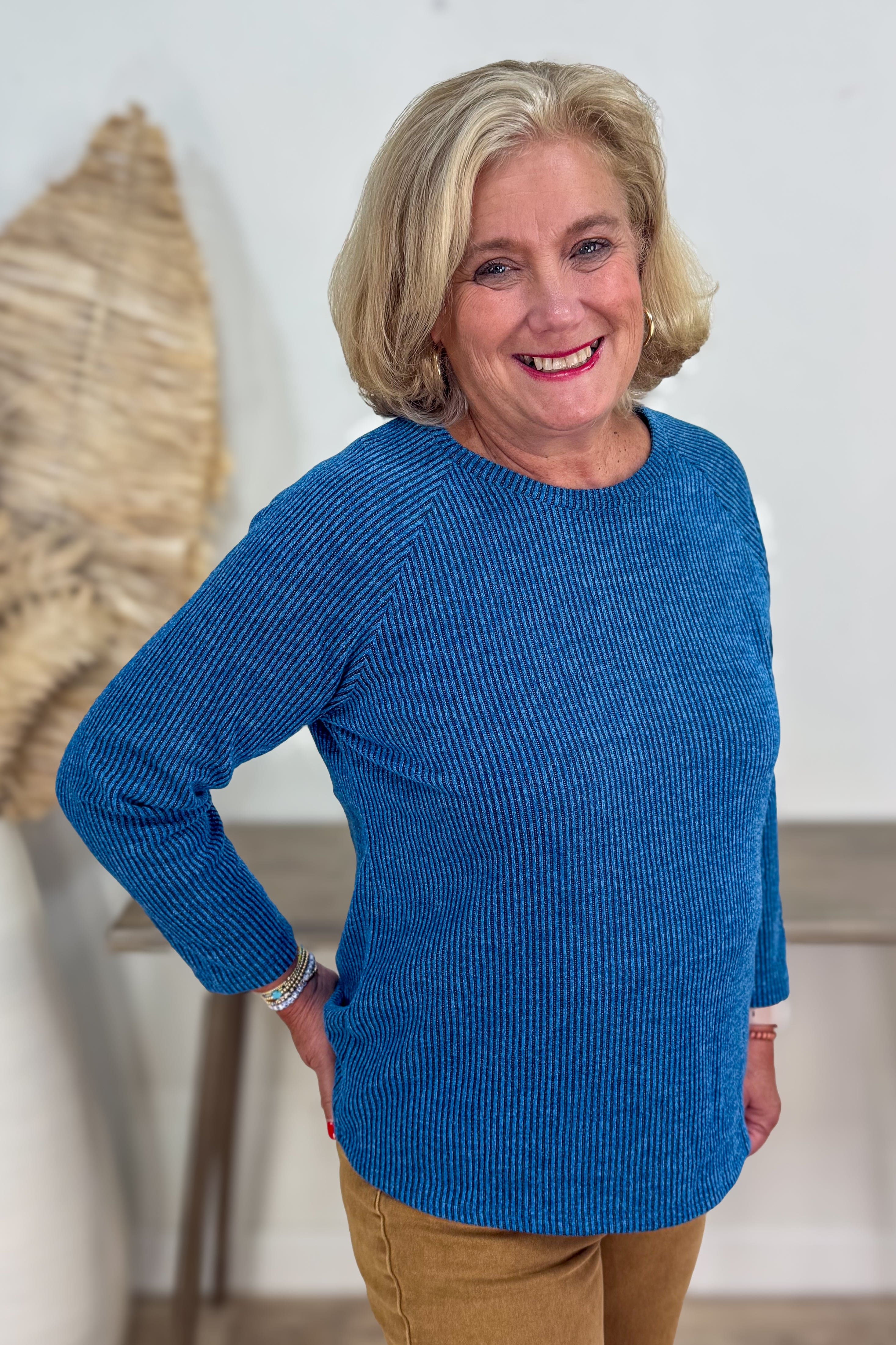 Woman wearing a blue sweater standing indoors with a neutral background