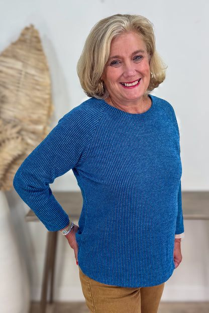 Woman wearing a blue sweater standing indoors with a neutral background
