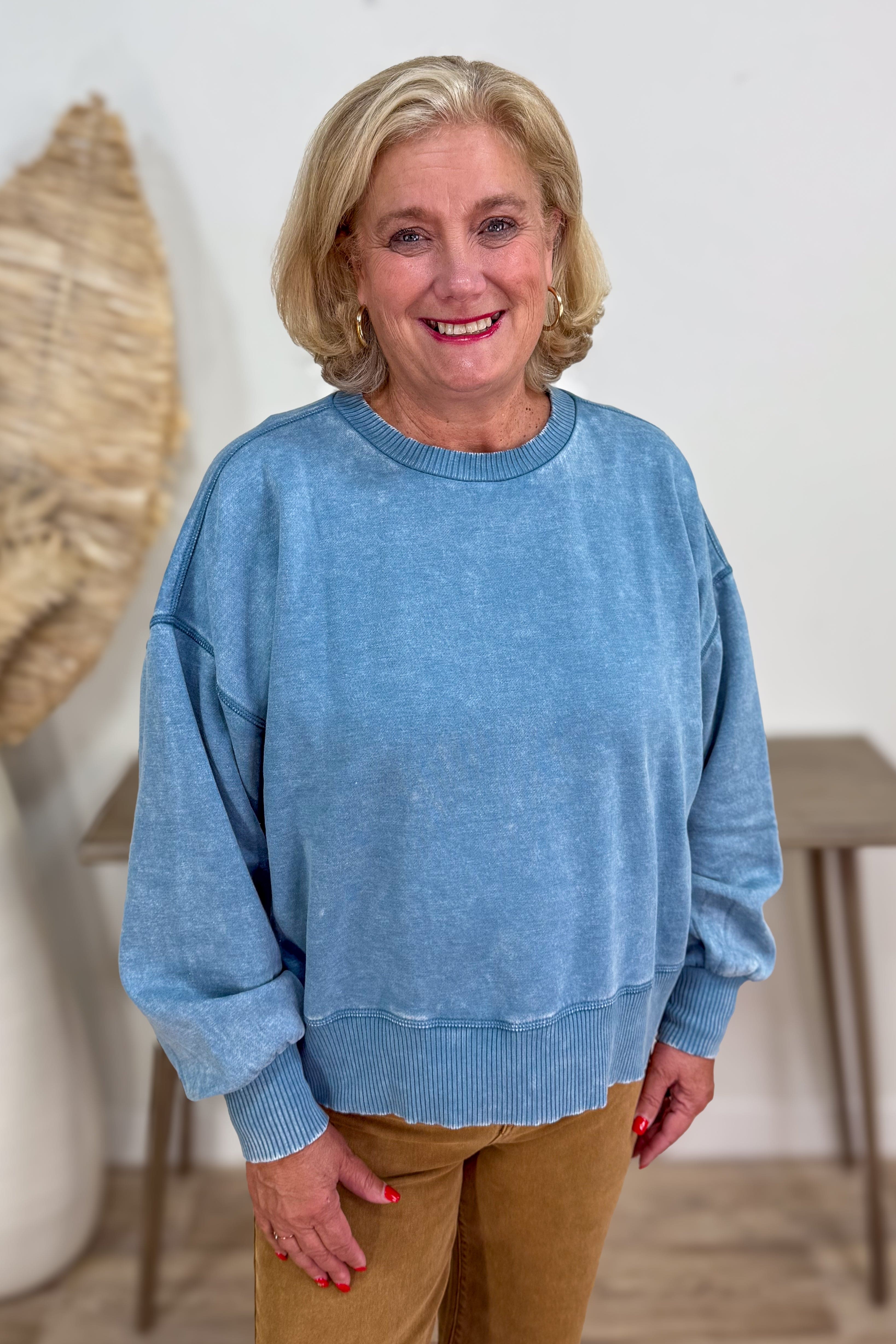 Woman wearing a blue sweater and brown pants indoors.