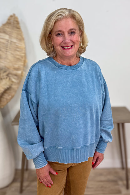 Woman wearing a blue sweater and brown pants indoors.
