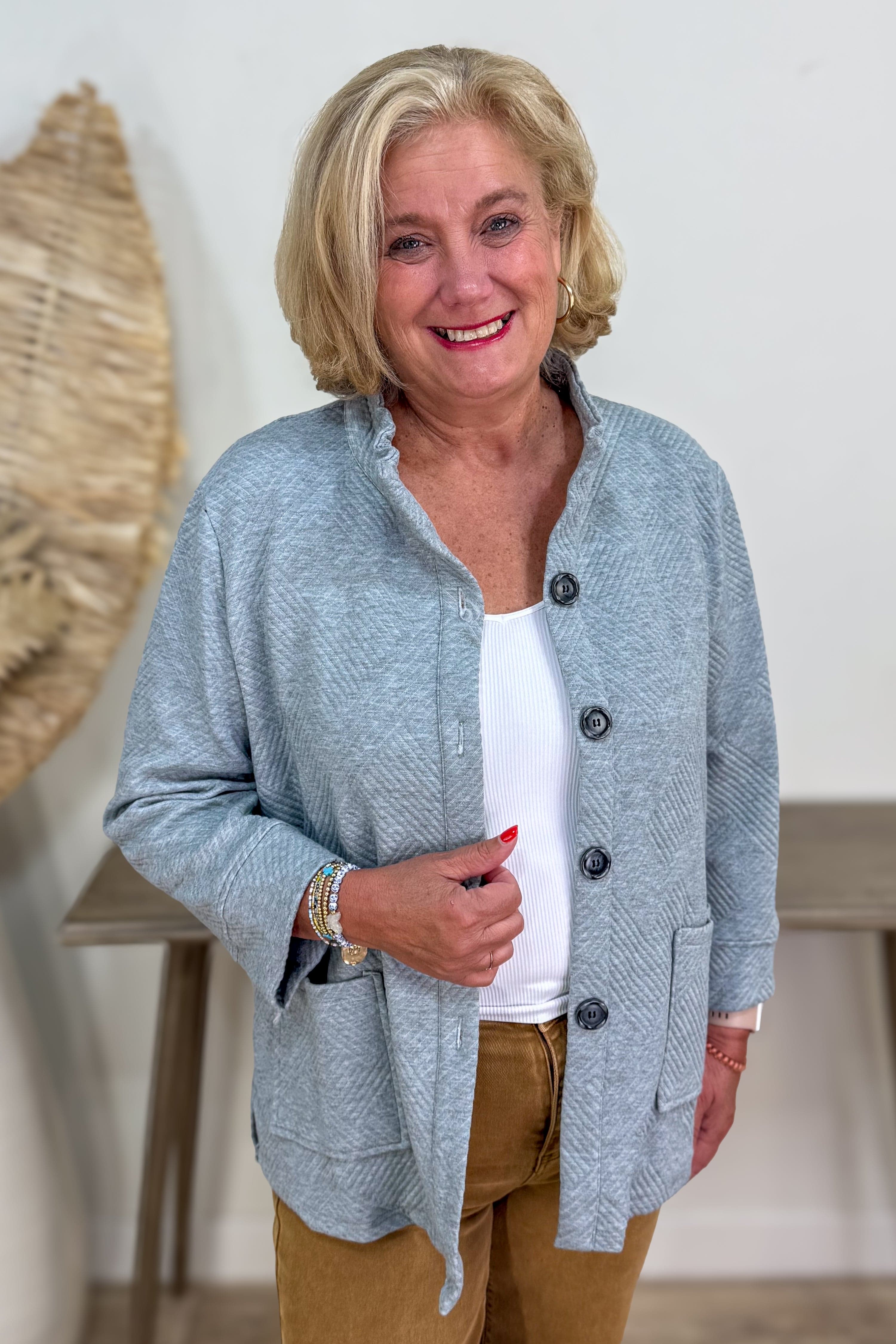 Woman wearing a gray cardigan over a white shirt with brown pants indoors.