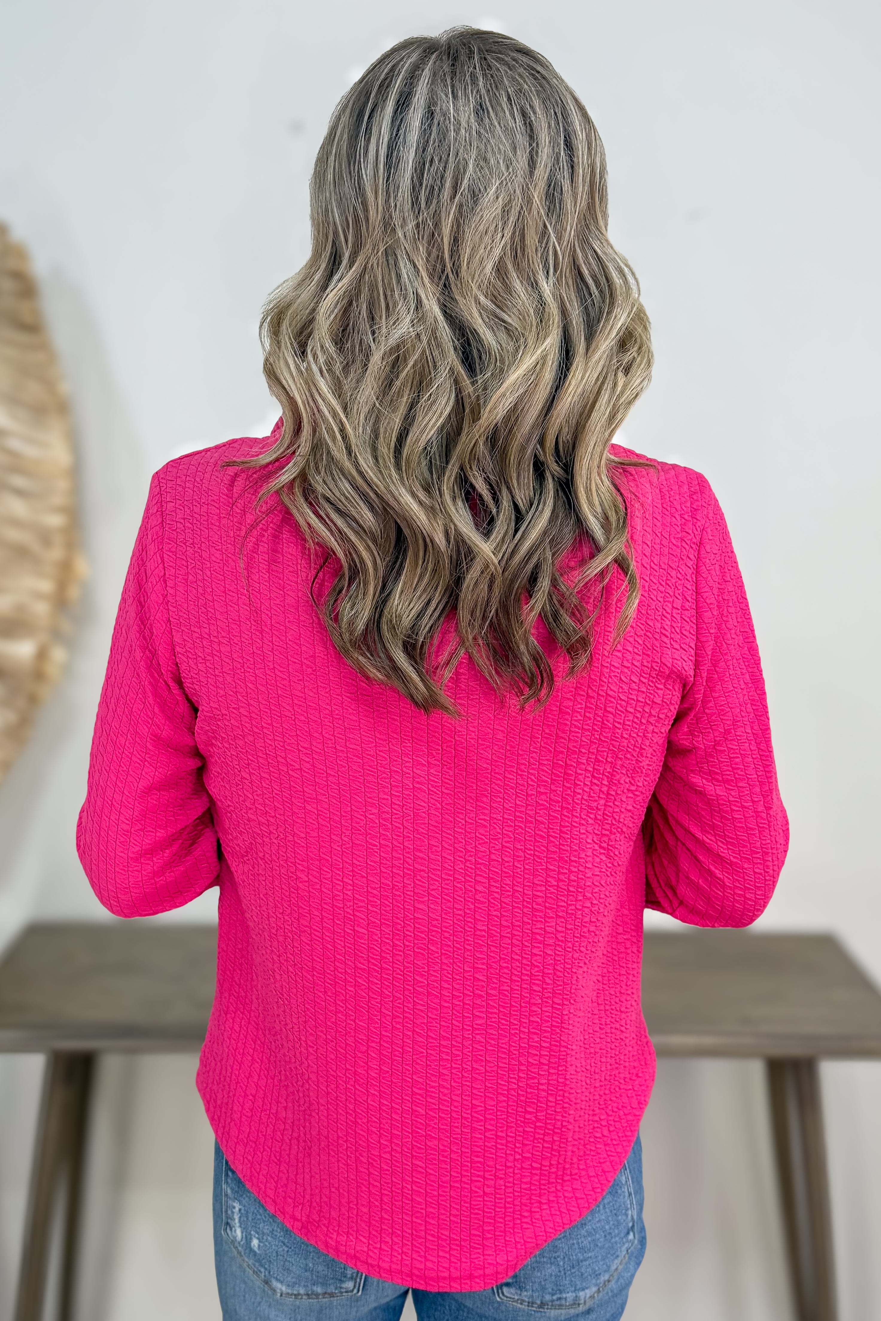 Person wearing a bright pink long-sleeve top with a neutral background