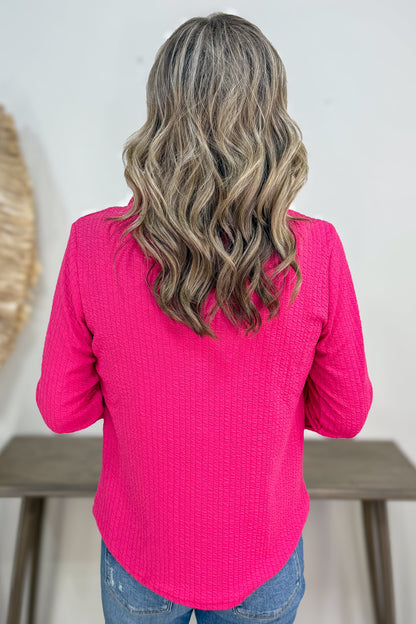Person wearing a bright pink long-sleeve top with a neutral background