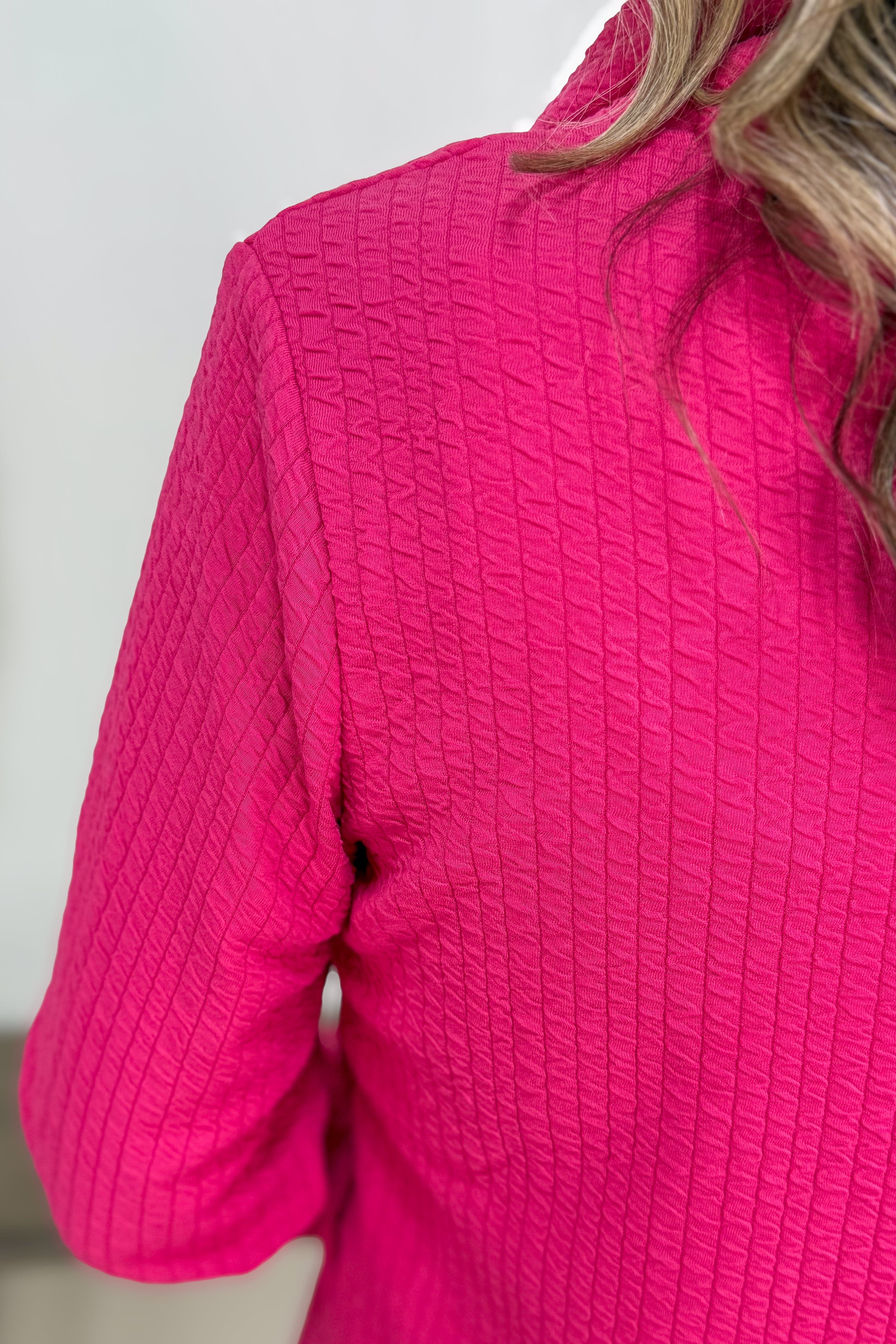 Close-up of a bright pink textured jacket worn by a person.