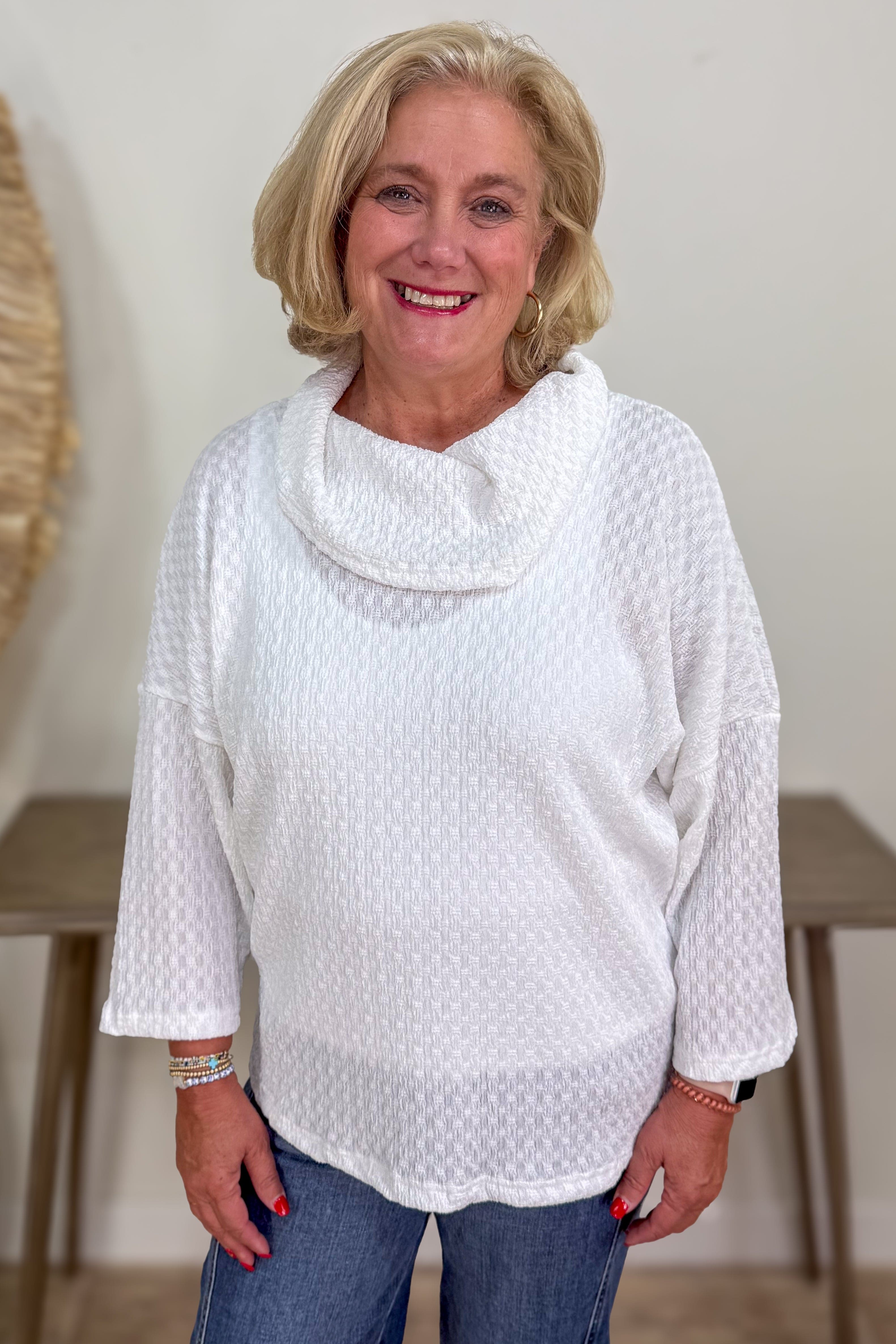 Woman wearing a white textured top and blue jeans indoors.