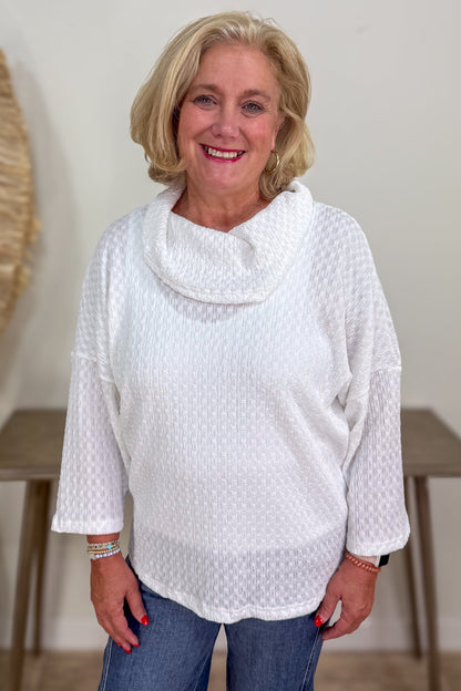 Woman wearing a white textured top and blue jeans indoors.