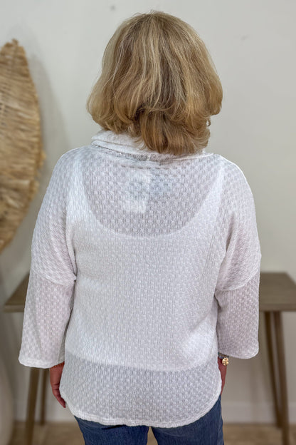 Person wearing a light gray textured blouse with a white wall background