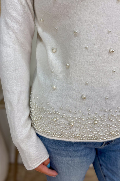 Gray sweater with pearl embellishments worn by a person, blurred background