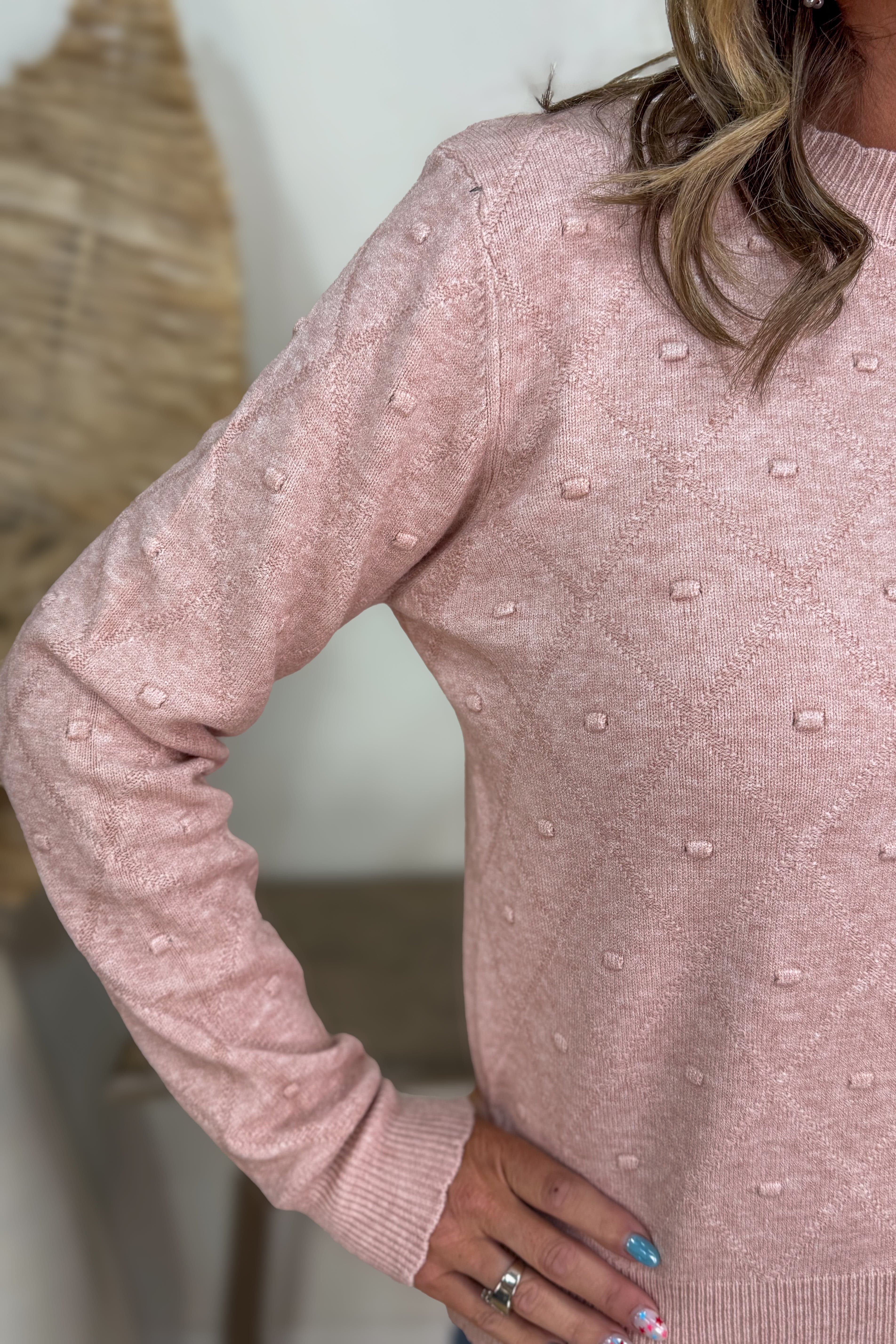Pink sweater with textured pattern worn by a person, blurred background