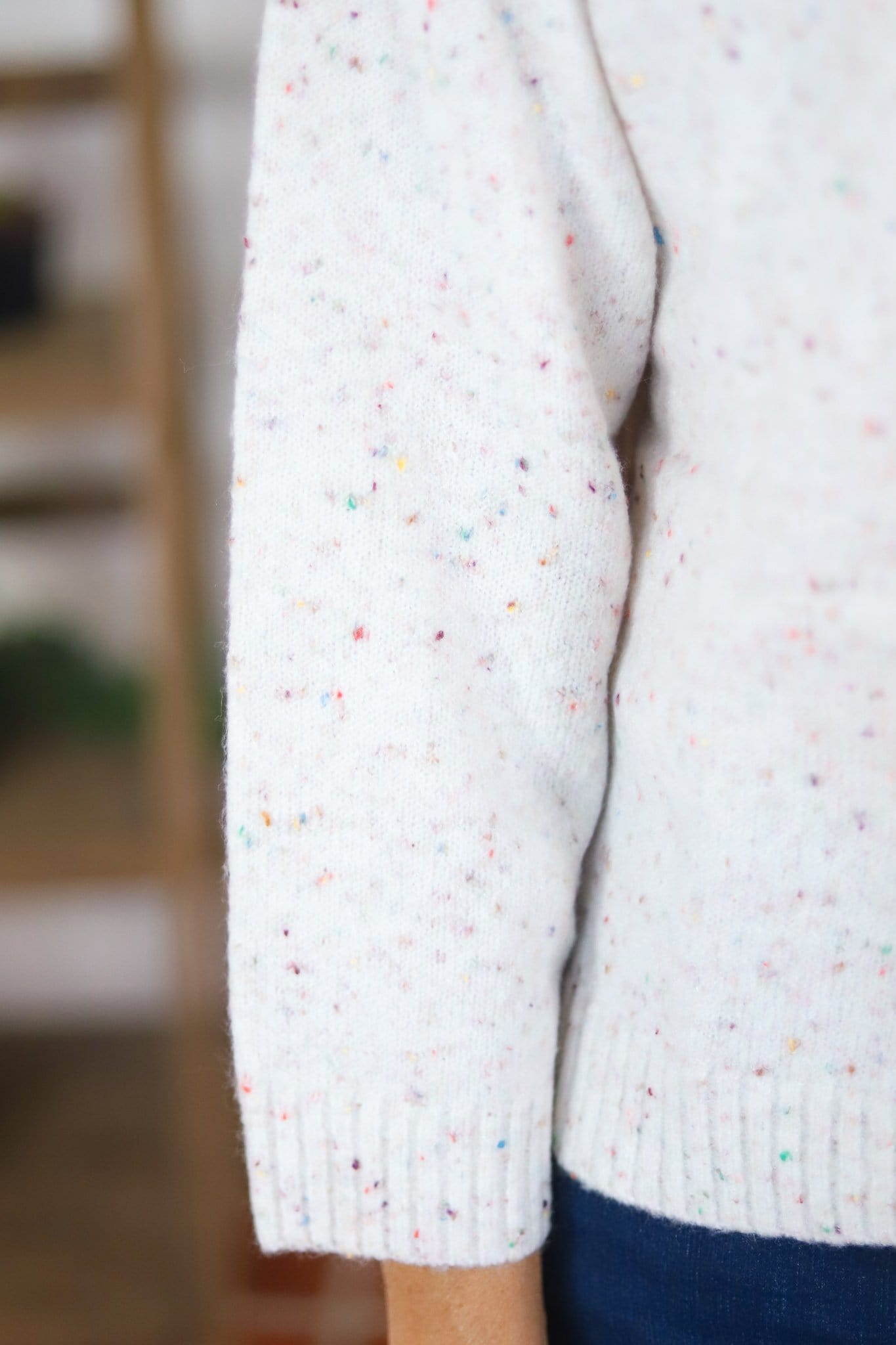 sleeve of white button up sweater with color specks in fabric